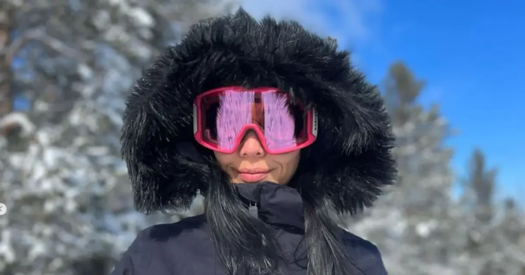 woman with pink ski glasses and black jacket in the snow